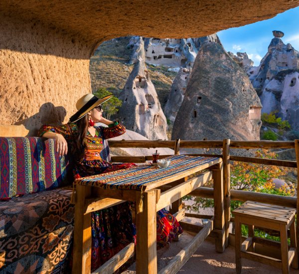 Woman in Bohemian dress sitting on traditional cave house in Cappadocia, Turkey.